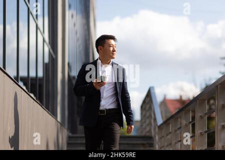 Der Chef des asiatischen Geschäftsmannes schaut auf das Mobiltelefon und liest Nachrichten vom Telefon und schreibt in einen Boten außerhalb des Büros Stockfoto