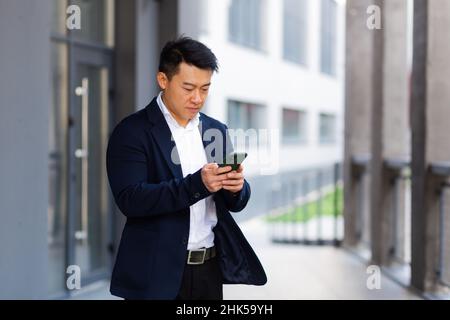 Der Chef des asiatischen Geschäftsmannes schaut auf das Mobiltelefon und liest Nachrichten vom Telefon und schreibt in einen Boten außerhalb des Büros Stockfoto