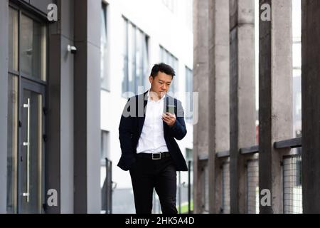 Der Chef des asiatischen Geschäftsmannes schaut auf das Mobiltelefon und liest Nachrichten vom Telefon und schreibt in einen Boten außerhalb des Büros Stockfoto