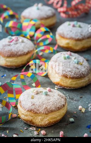 Krapfen, Berliner oder Donuts mit Streamer, Konfetti und Mini-Marschmalchen auf grauem Hintergrund. Farbenfrohes Karnevals- oder Geburtstagsbild, vertikal Stockfoto