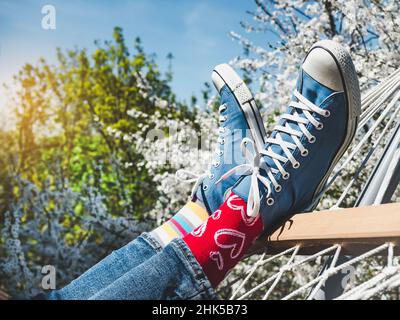 Trendige Sneaker und bunte Socken auf dem Hintergrund eines blühenden Baumes. Nahaufnahme, im Freien. Tageslicht. Männer- und Damenstil. Schönheit und Eleganz c Stockfoto