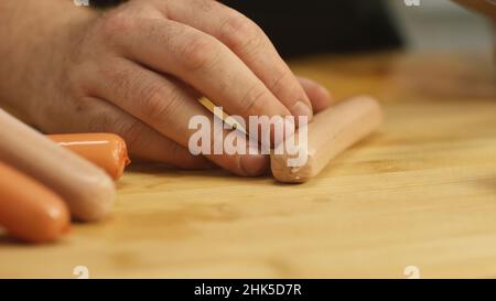 Nahaufnahme von Menschenhänden, die mit einem Küchenmesser Würstchen auf einem Holzschneidebrett schneiden. Zubereitung von Speisen. Stockfoto