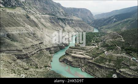 Luftaufnahme eines geschwungenen grünen Flusses, der zwischen Felshängen fließt. Aktion. Sommer Naturlandschaft mit einem malerischen Bach und Bergkette Stockfoto