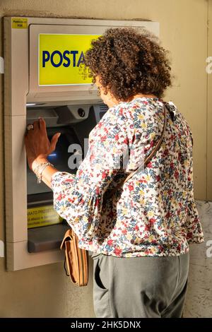 29. August 2021, Vicenza, Italien:Frau mittleren Alters, die am Geldautomaten der italienischen Post Geld von ihrer Kreditkarte abzieht Stockfoto