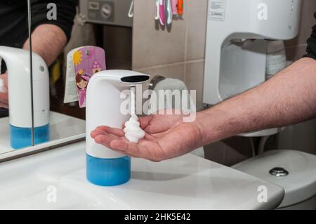 Seifenspender spritzt Schaum in einer männlichen Hand Stockfoto