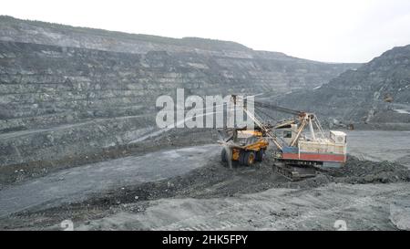 Bagger füllt Muldenkipper mit Erde im Tagebau. Schwere Maschinen arbeiten in der Bergbauindustrie im Tagebau. Stockfoto
