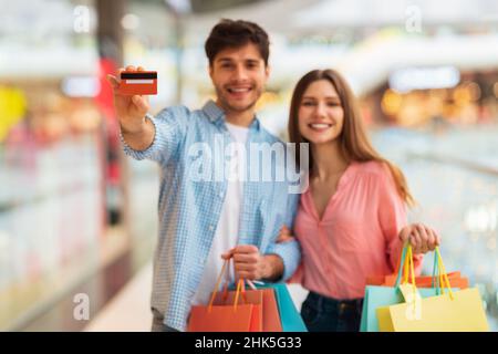 Glückliches Paar Einkaufen Und Zeigen Kreditkarte In Mall Indoors Stockfoto