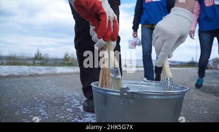 Hände tauchen Farbe in einen vollen Farbbecher. Clip. Nahaufnahme eines Arbeiters seinen Pinsel in die Farbe. Arbeiter in Blau tauchen den Pinsel in die Farbe. Stockfoto