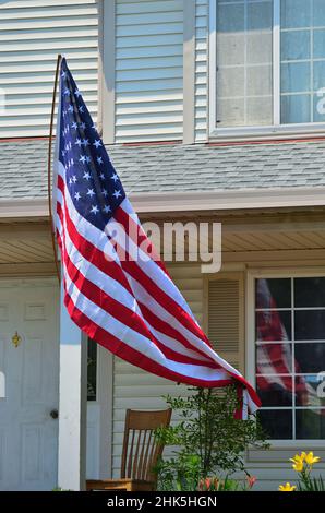 South Elgin, Illinois, USA. Eine amerikanische Flagge fliegt in der Nähe des Haupteingangs des Hauses und spiegelt sich in einem Fenster im ersten Stock wider. Stockfoto