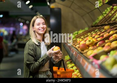 Junge blonde Frau wählt Obst Gemüse auf der Theke im Supermarkt. Weibliche Hausfrau einkaufen auf dem Markt in der Nähe von Gemüse Departme Stockfoto