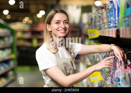 Porträt einer Verkäuferin, einer lächelnden Frau und einem Blick auf die Kamera im Supermarkt. Angenehme freundliche Verkäuferin im Laden zwischen den Reihen stehen. T Stockfoto