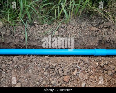 Das kleine PVC-Rohr liegt im Graben in der Nähe des Pflasters für das Wasserversorgungssystem des ländlichen Dorfes, Vorderansicht mit dem Kopierraum. Stockfoto