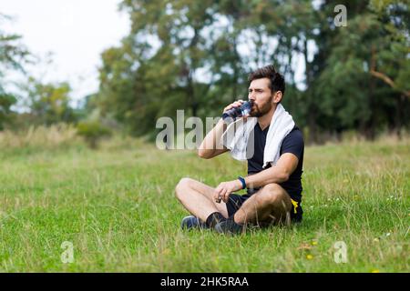 Müde erschöpft dehydriert Athlete Mann Läufer Trinkwasser Flasche nach dem Training. Sportflasche Getränk. Männlicher Sportler. Läufer verschwitzt und durstig afte Stockfoto