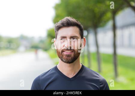 Nahaufnahme Porträt junger, glücklicher bärtiger Mann, der in der Natur zwischen Waldbäumen steht, entspannt, atmet frische Luft und schließt die Augen. Männlich genießt ein Leben von Stockfoto