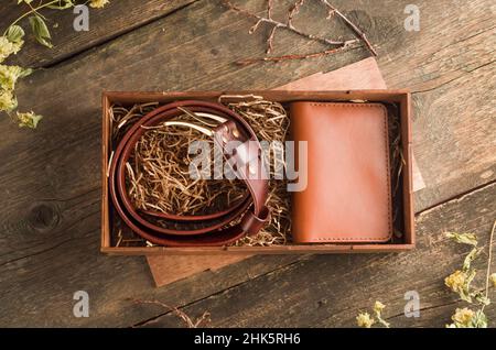 Handgefertigtes Geschenkset für einen Mann mit einem Ledergürtel und einem braunen Visitenkartenhalter in einer Schachtel auf einem alten Vintage-Holzhintergrund. Stockfoto