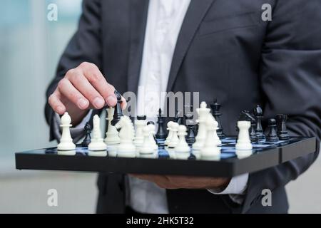 Nahaufnahme eines erfolgreichen Geschäftsmannes, der ein Schachbrett hält und einen Schritt macht Stockfoto