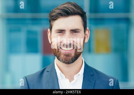 Porträt eines jungen, gutaussehenden Mannes mit Bart, eines Geschäftsmanns, der die Kamera anschaut und ein lächelndes Nahaufnahme-Foto zeigt Stockfoto