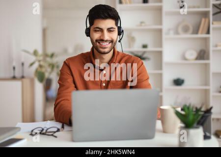 Arabischer Mann mit Laptop und Headset am Schreibtisch Stockfoto