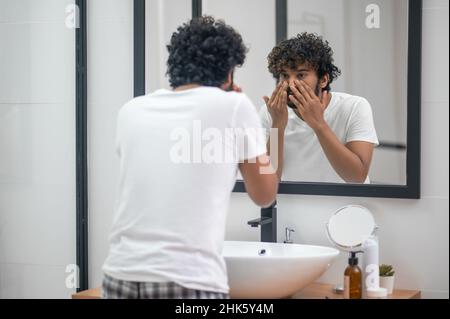 Konzentrierter junger Mann, der seine Gesichtshaut untersucht Stockfoto