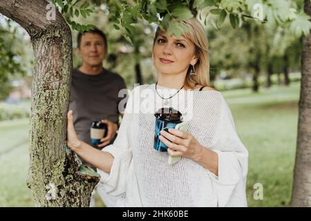 Ein erwachsenes, reifes, glückliches Paar in Liebe umarmt sich im Stadtpark. Ein blonder Kaukasusmann und eine blonde Frau verbringen Zeit miteinander und trinken Kaffee. Senior Stockfoto