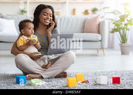 Remote Business. Happy Black Woman Mit Baby Arbeitet Mit Laptop Und Handy Stockfoto