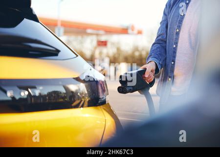 Mann, der ein Elektroauto mit einem Schnellladegerät an einer EV-Ladestation einsteckt Stockfoto