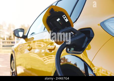 Nahaufnahme der Stromversorgung, die an ein Elektroauto angeschlossen ist, das mit einem Schnellladegerät aufgeladen wird Stockfoto