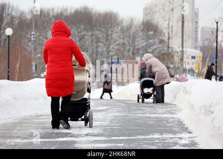 Frauen, die mit Kinderwagen auf einer Straße spazieren. Mütter in der Winterstadt, Freizeit bei Schneewetter Stockfoto