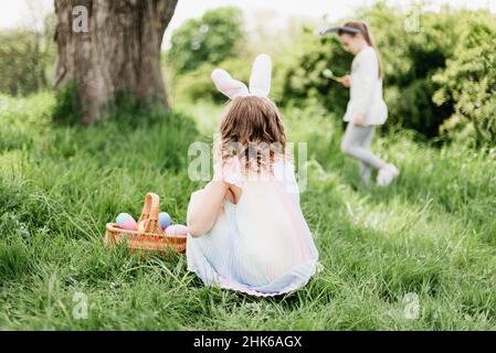 Ostereiersuche. Eine Gruppe von Kindern mit Hasenohren läuft auf der Ostereiersuche im Garten, um bunte Eier abzuholen. Ostertradition Stockfoto