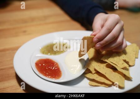 Person, die Nachos in Sauce im Restaurant eintaucht Stockfoto