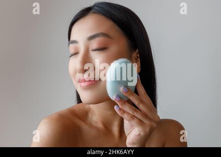 Asiatische Frau, die im Studio ein reinigendes Gesichtsmassager verwendet Stockfoto