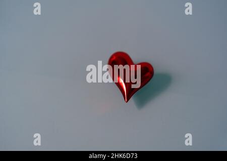 Isoliertes rot glänzendes Herz auf blauem Glashintergrund. Platz für Text kopieren. Stockfoto