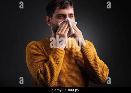 Nahaufnahme eines Mannes, der seine Nase mit einem Taschentuch bedeckt, das sich schlecht fühlt und ein kaltes Gesundheitskonzept erwischt. Stockfoto