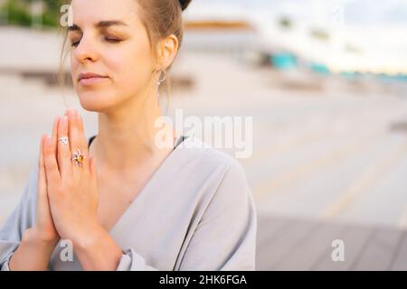 Nahaufnahme einer meditativen jungen Frau, die im Stadtpark Yoga praktiziert und Namaste-Pose mit geschlossenen Augen ausführt. Stockfoto