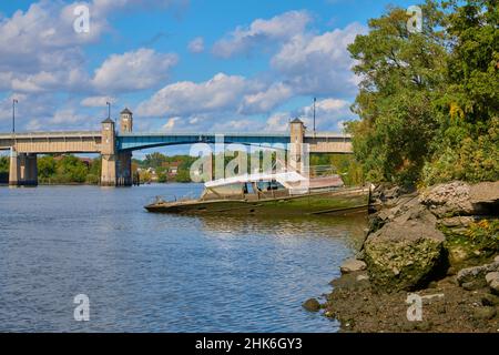 Halb versunkenes, geerdetes Vintage-Kabinenboot. Am Ufer des Hackensack River in New Jersey, USA. Blick Richtung Norden auf die Zugbrücke auf der Winant Avenue Stockfoto