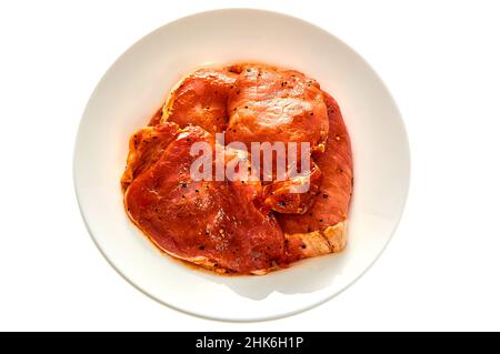 Schweinefleisch in Marinade liegt auf einem weißen Teller auf einem weißen isolierten Hintergrund Stockfoto