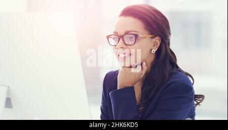 Positive Gedanken. Eine kleine Aufnahme einer attraktiven jungen Geschäftsfrau, die im Büro an ihrem Computer arbeitet. Stockfoto