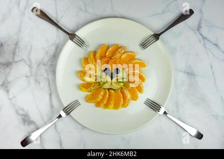 Lustige Löwengesicht-Komposition mit Früchten wie orangefarbener Blaubeere auf Marmortisch mit Gabeln Stockfoto