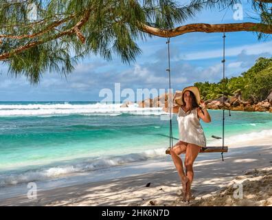 Attraktive junge Frau in Strandkleidung, sitzt auf Schaukel am paradiesischen Strand auf der tropischen Insel Stockfoto