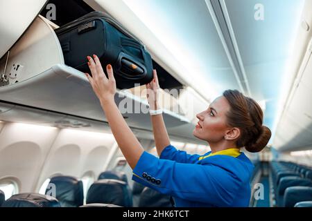 Stewardess, der Reisekoffer im Flugzeug in den Gepäckraum über dem Kopf stellt Stockfoto