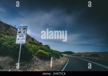 Schild „DRIVE ON LEFT IN AUSTRALIA“ auf der Straße im Hintergrund des dunklen Himmels Stockfoto