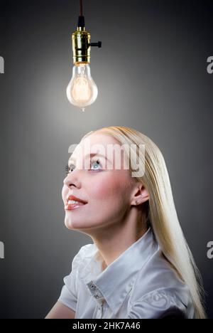 Junge blonde Frau betrachtet hängende beleuchtete Edison-Glühbirne Stockfoto