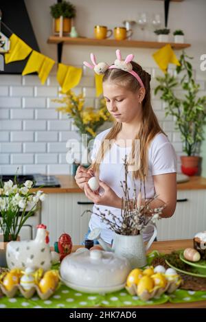 Mädchen 12 Jahre alt malt Eier für Ostern in der Küche. Stockfoto