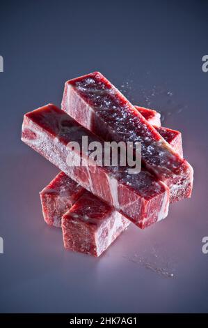 Rechteckige Schnitte von gefrorenem Rindfleisch auf dunklem Hintergrund gestapelt Stockfoto