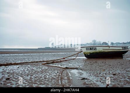 Bei Ebbe ruht auf dem Sand ein einflüchtiges Ruderboot. Harwich Low Lighthouse und Maritime Museum können im Hintergrund während des Winters Essex, Großbritannien, gesehen werden Stockfoto