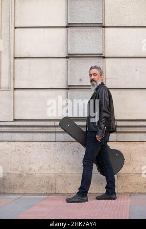 Senior Mann in Lederjacke trägt E-Gitarre im Freien Stockfoto