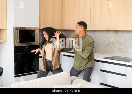 Glückliches junges multirassisches Paar in der Liebe tanzt in der Küche. Fröhlicher Freund und Freundin mit Spaß zu Hause. Neuvermählte zog in eine neue Wohnung Stockfoto