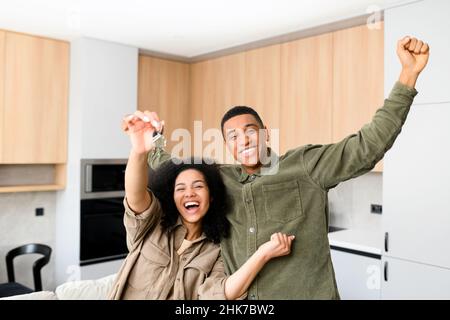 Ein verliebter multirassischer Partner umarmt sich in einem neuen Zuhause, während er die Schlüssel in den Händen hält. Junge multirassische Familie kaufte ein neues Haus, mieteten eine Wohnung, bekam eine Hypothek Stockfoto