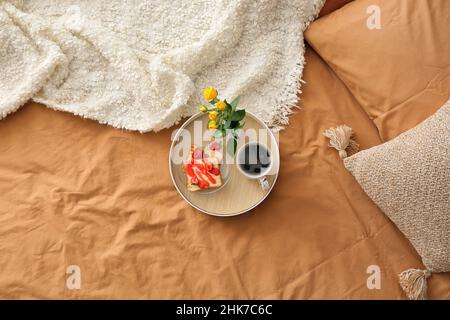 Tablett mit leckerem Frühstück und schönen Blumen auf einem bequemen Bett Stockfoto