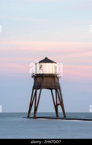 Nahaufnahme des Dovercourt Low Lighthouse in Harwich & Dovercourt, North Essex, Großbritannien. Die untergehende Sonne wirft einen rosa Schein über den Abendhimmel. Stockfoto